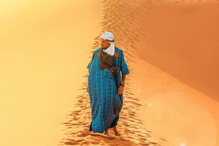 A guide in blue traditional clothing standing on a sand dune