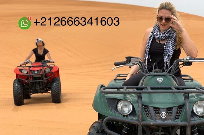 Two helmeted travelers seated on a quad with orange dunes behind them