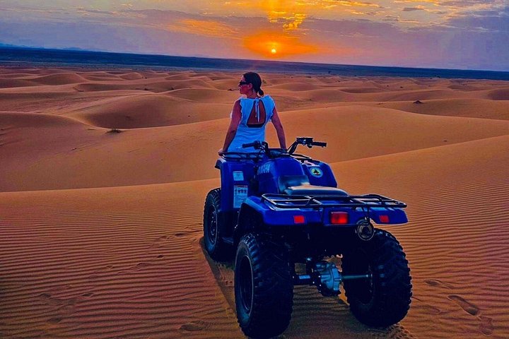 A traveler seated on a blue quad overlooking dunes at sunset