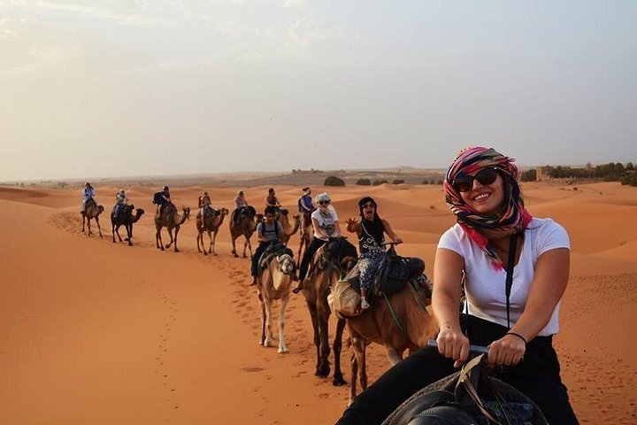 Travelers riding a camel caravan across sand near Merzouga