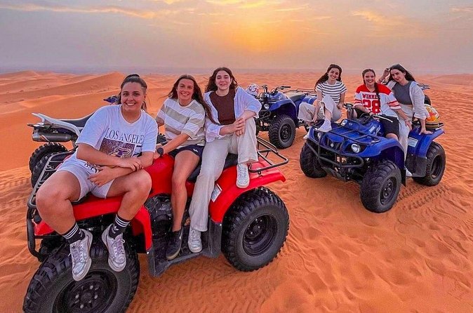 A group of travelers posing with parked quad bikes on desert sand